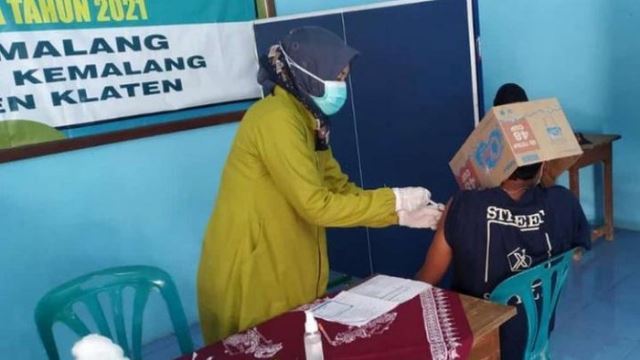 scared of getting vaccinated, young man in indonesia covers his whole face with cardboard box
