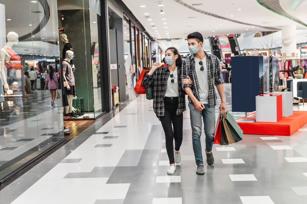 Young couple wearing masks and carrying shopping bags in shopping mall