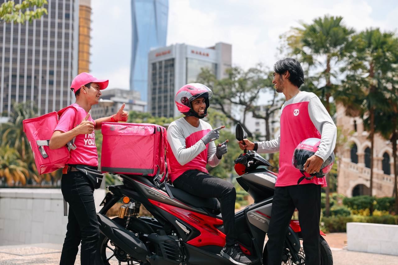3 happy foodpanda riders in uniform chatting with each other
