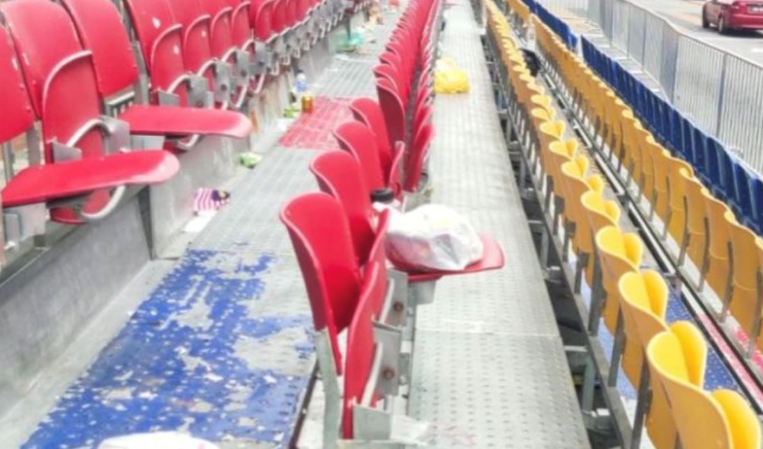 post-merdeka parade scene: grandstand littered with bottles, leftover food, and flags