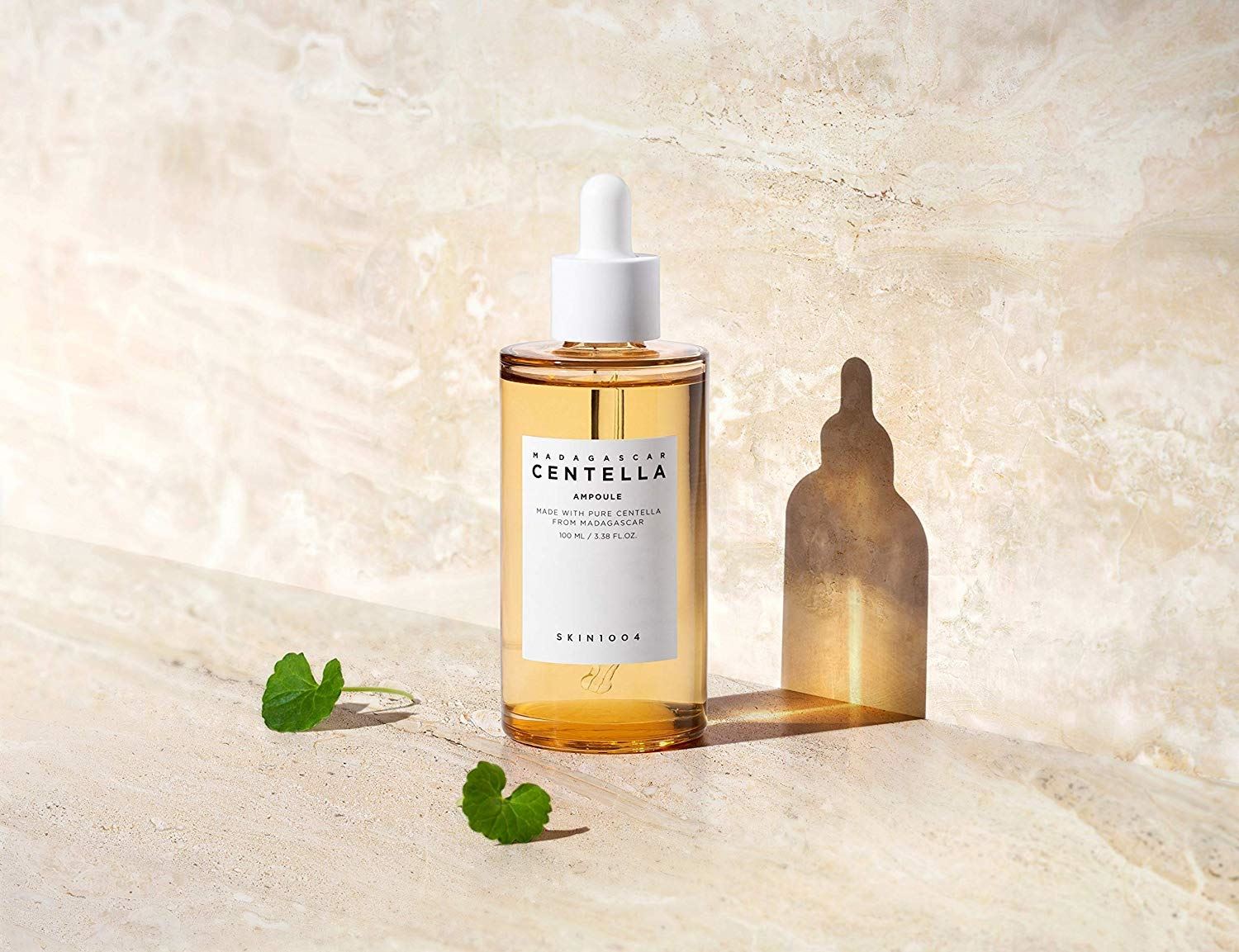 A bottle of serum with leaves beside it and a reflection behind it