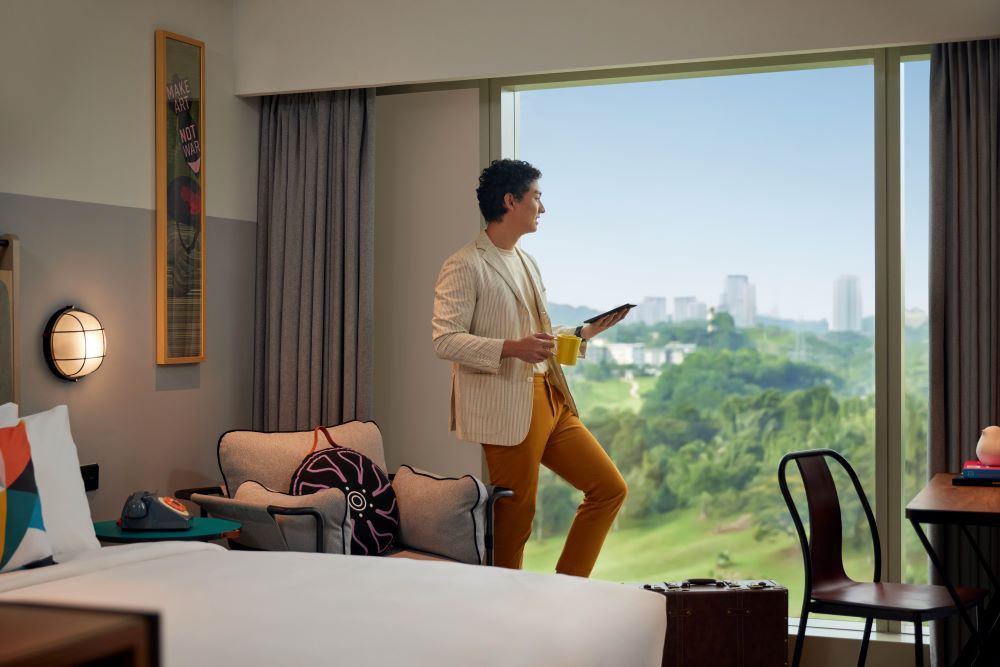 A man standing by the window of a hotel at Moxy Putrajaya