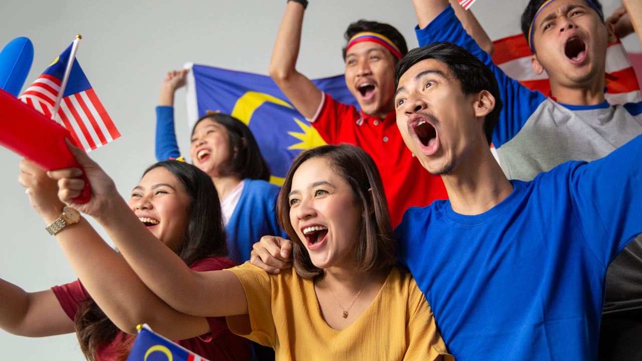 Malaysians cheering while holding the Malaysian flag