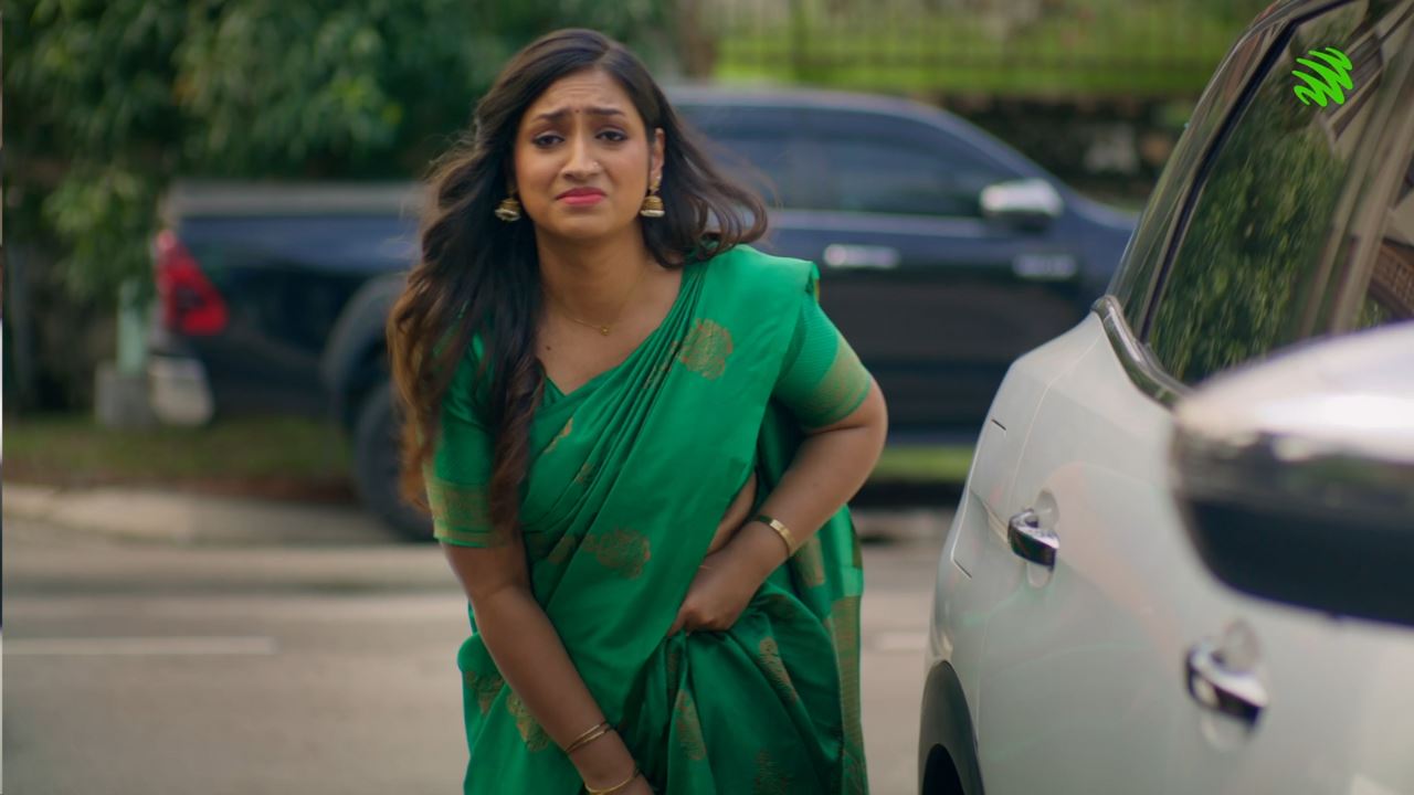 A distressed Indian woman who's holding onto her green saree that has come undone.