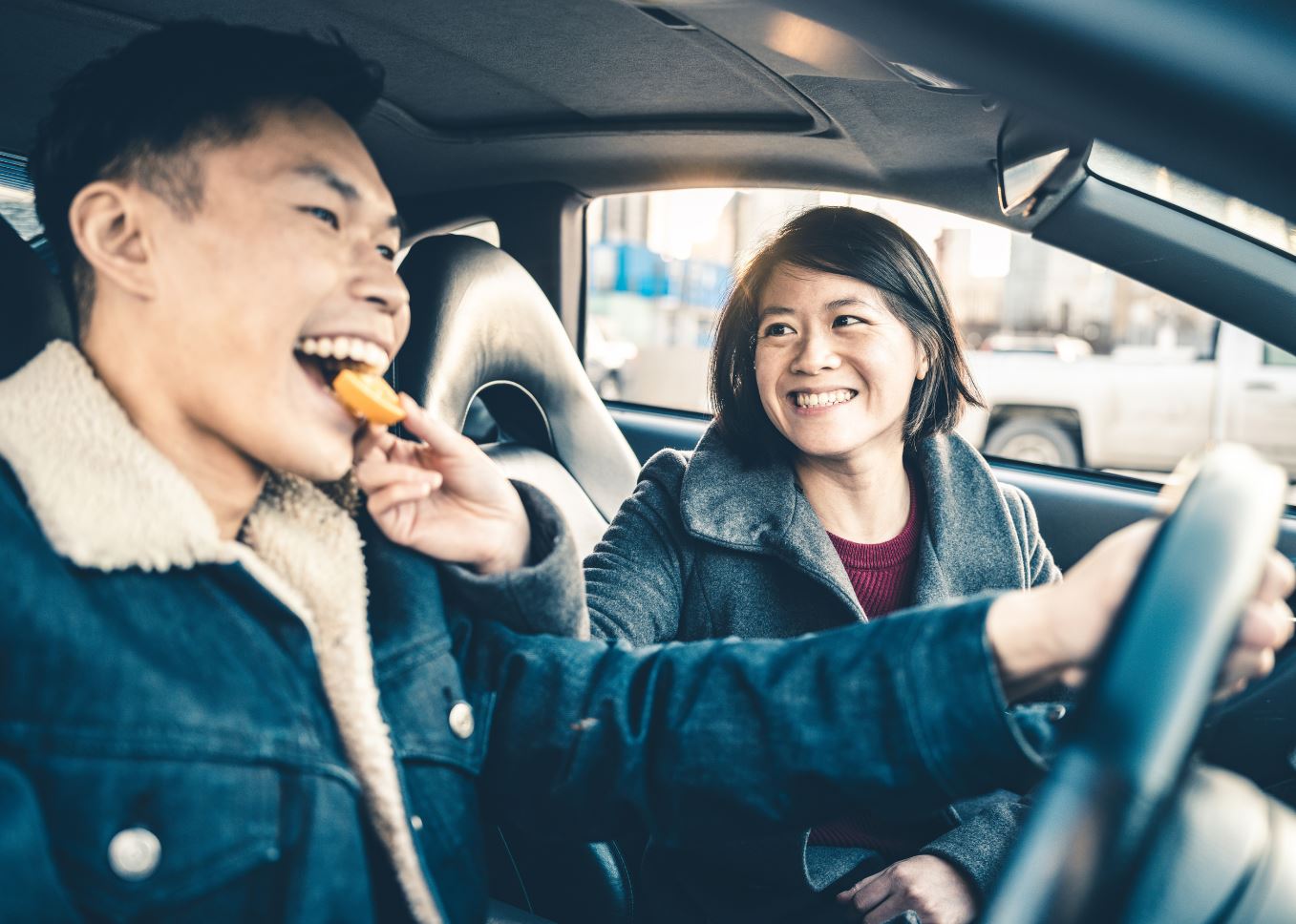 A woman feeding a man a snack while he drives
