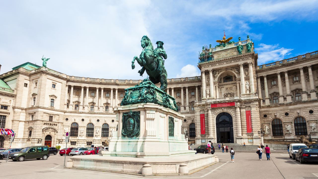 A statue in front of the Hofburg Imperial Palace in Vienna, with cars and people around