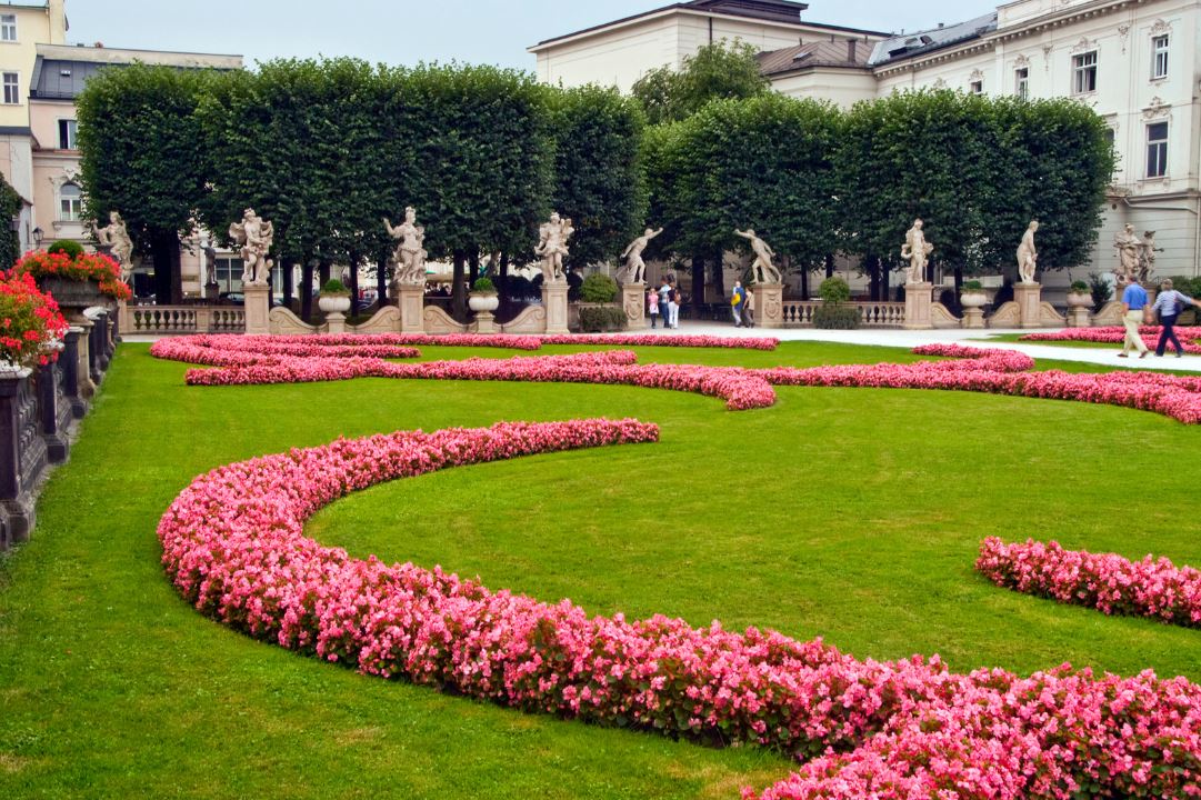 A garden with flowers and statues and a pathway for people to walk in Salzburg
