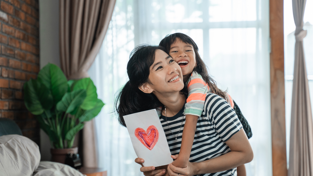 ibu mendukung anak perempuan sambil pegang lukisan gambar hati